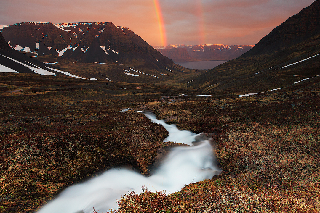 En dobbelt regnbue rækker over en fjord ved Vestfjordene på en solrig dag i den Islandske sommer.