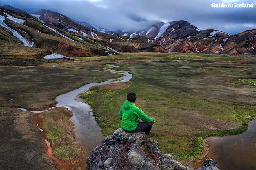 Ein Mann sitzt und schaut auf die Landschaft in Landmannalaugar