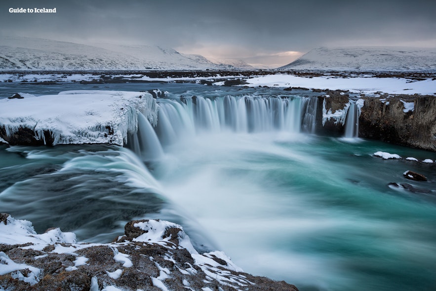 Snow and ice partially cover the Godafoss waterfall in winter.