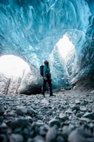 A person admires intricate ice patterns inside an ice cave as light streams in from above.