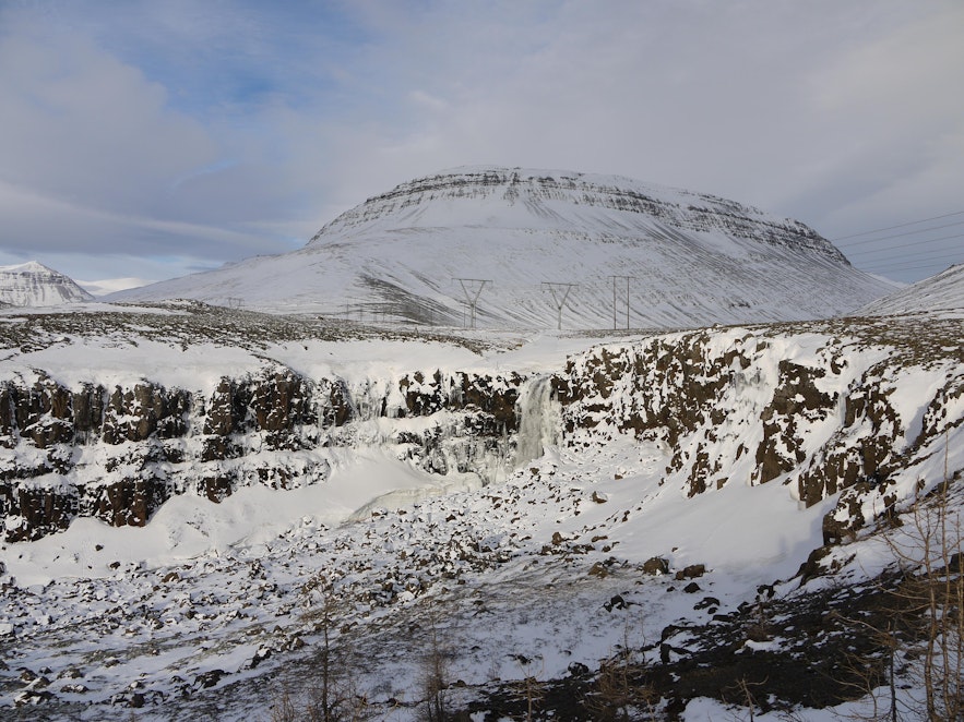 Snow and ice cover the landscapes surrounding Budararfoss waterfall in winter.