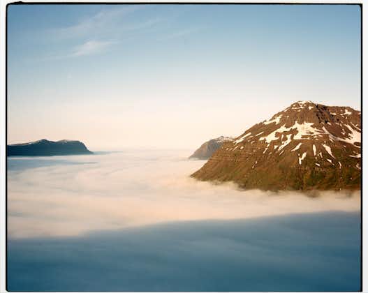 A sunset view of Mount Bjolfur on the Seydisfjordur fjord looking down on a soft blanket of cloud.
