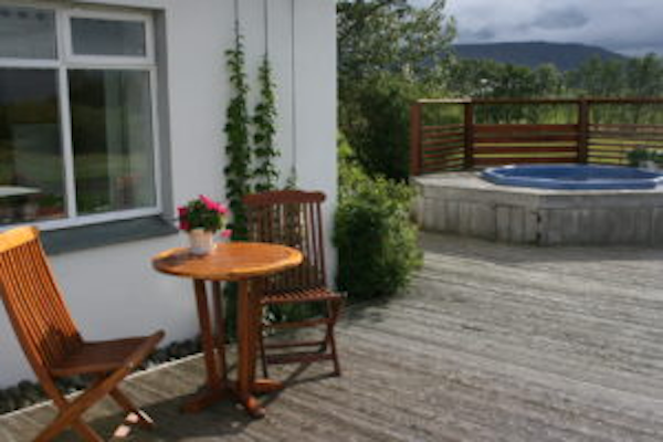 The outside area at Jadar Farm with a wooden table and two chairs, and a hot tub in the background.