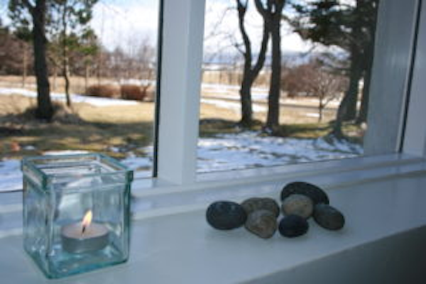 A lit candle and a pile of pebbles on a window sill at Jadar Farm.