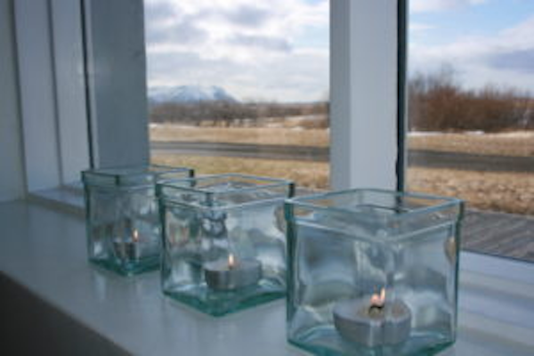 Three glass tealight holders with lit candles inside on the windowsill at Jadar Farm accommodation in West Iceland.