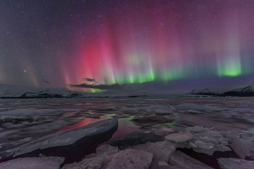 Las auroras boreales llenan el cielo y tiñen el entorno de sus colores, particularmente en la laguna glaciar Jökulsárlón.