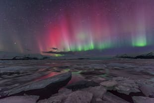 Norrskenet täcker himlen och färgar den omgivande landskapet med sina skiftande nyanser, särskilt över issjön Jökulsárlón.