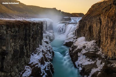 Gullfoss waterfall on Iceland's Golden Circle looks stunning with a splattering of snow and the orange glow of the sunset in the background.