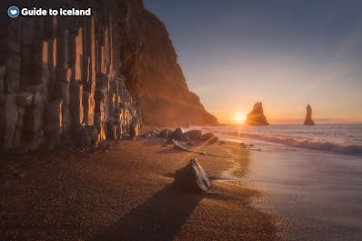 Reynisfjara beach looks mesmerizing at sunset with its basalt columns lining the shore and Reynisdrangar sea stacks standing proudly in the ocean.