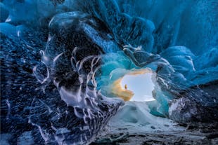 Jasny zimowy dzień jest widoczny przez wejście do jednej z krystalicznie błękitnych jaskiń lodowcowych Vatnajökull.