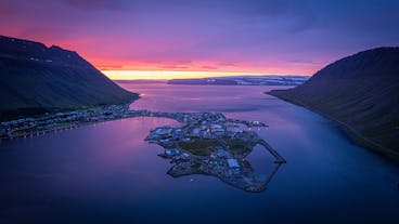 An aerial view of the coastal town of Isafjordur, with the sky lit up pink and purple at sunset.