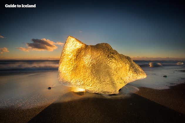 Ein Eisberg an dem atemberaubenden Diamantstrand an der Südküste Islands in goldenes Licht getaucht.