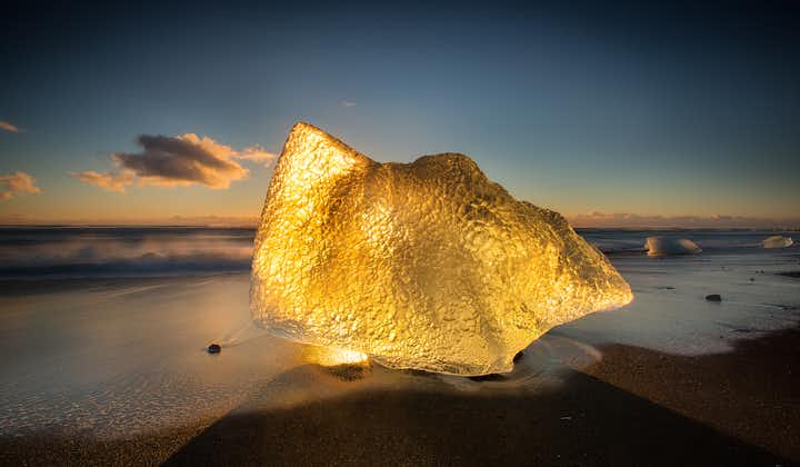 En gylden glød oplyser et isbjerg på sydkysten af Island ved den utrolige Diamantstranden.
