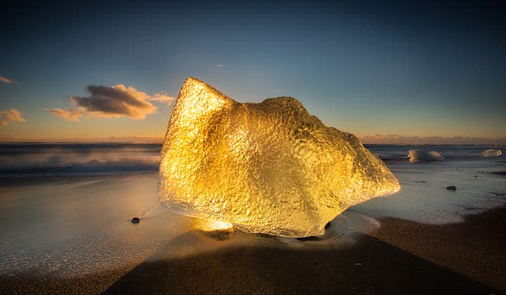En gyllene glöd lyser upp ett isberg på den isländska sydkusten vid den otroliga Diamantstranden.