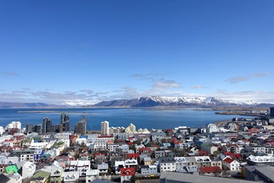 Dachy Reykjaviku z widokiem na wybrzeże i góry w oddali.