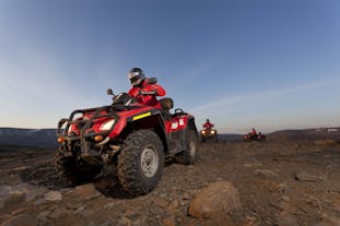 People drive ATVs over Iceland's rugged terrain with a backdrop of snowy mountains.