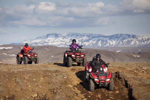 People drive ATVs over Iceland's rugged terrain with a backdrop of snowy mountains.
