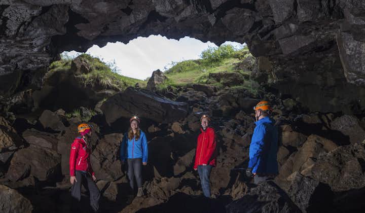 People wearing helmets and flashlights stand inside a lava cave with the light shining in from above.