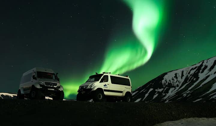 A display of the northern lights shines over two super jeeps in Iceland.