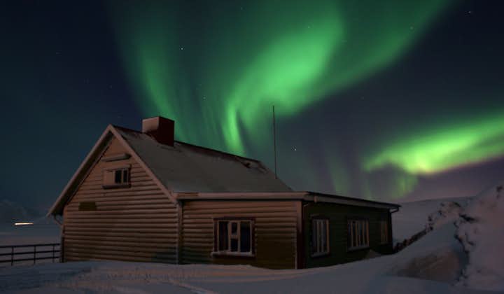 The aurora borealis dancing over a countryside cottage.