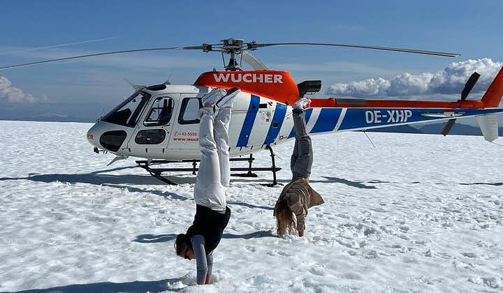 Two travelers doing a headstand beside a helicopter during a glacier landing.