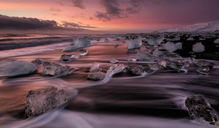 Aallot lyövät jäävuoriin Timanttirannalla auringon laskiessa.