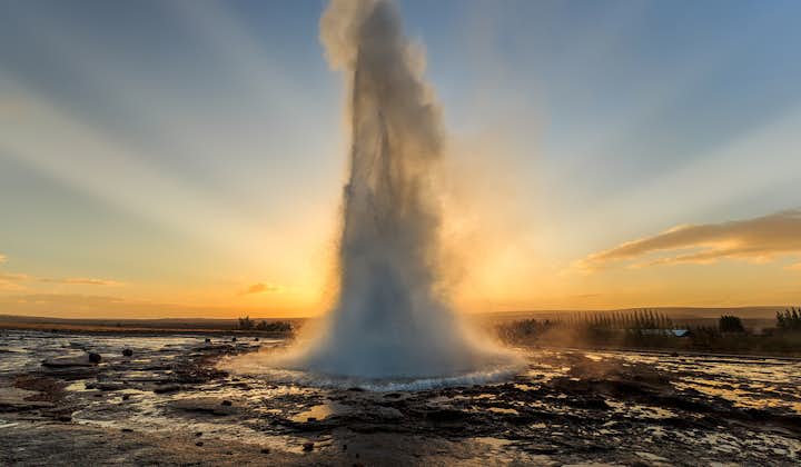 Strokkur the geyser erupts dramatically in front of the sunrise.