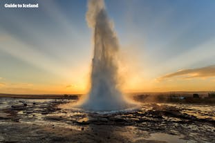 Strokkur the geyser erupts dramatically in front of the sunrise.