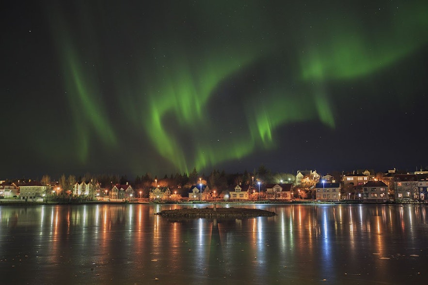 La aurora boreal sobre un estanque de la ciudad en Reikiavik, Islandia