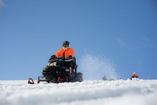 A person zooms across the Langjokull glacier on a snowmobile on a bright, blue-sky day.