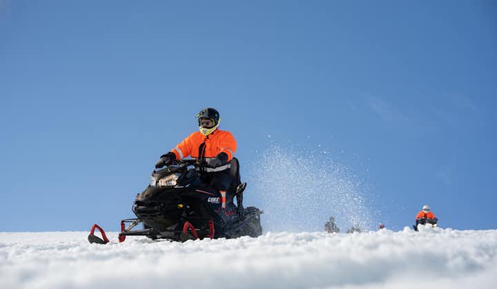 A person zooms across the Langjokull glacier on a snowmobile on a bright, blue-sky day.
