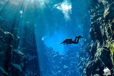 A diver floats in the mesmerizing blue waters of the Silfra fissure as the sunlight filters through from above.