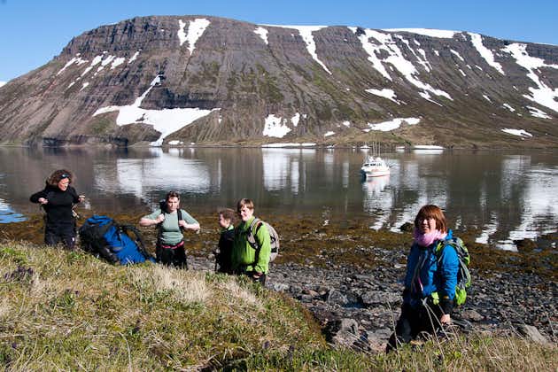 A group of people on a tour of the Hornstrandir Nature Reserve stand in front of a fjord with a boat in it.