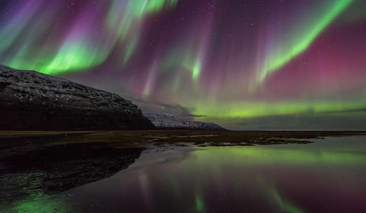Above a beautiful lake in Iceland, emerald and violet Northern Lights dance across the sky.