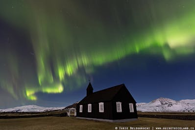 แสงเหนือเลื้อยส่ายอยู่บนท้องฟ้าช่วงคืนหน้าหนาวเหนือโบสถ์สีดำปูดิร์ในไอซ์แลนด์ตะวันตก