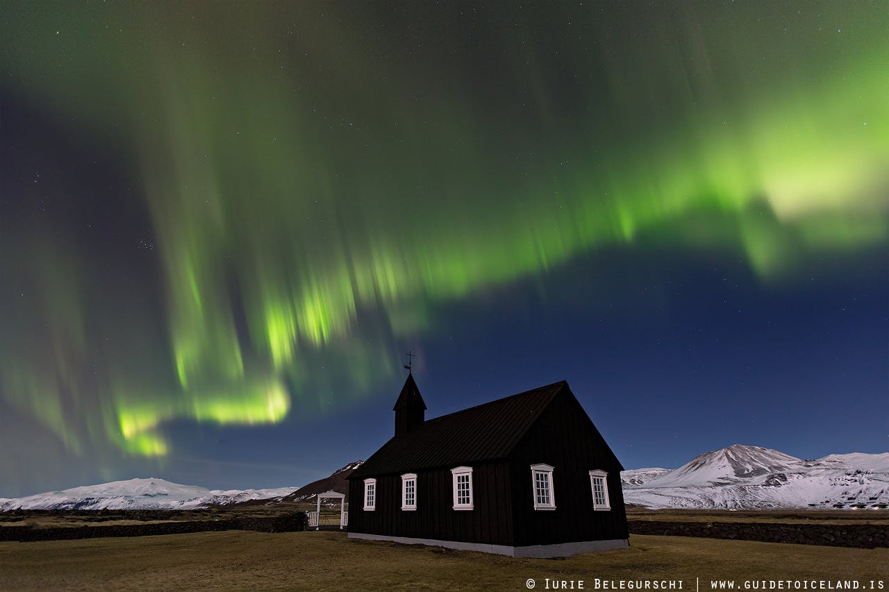 Ovanför den svarta kyrkan i Buðir på västra Island ringlar sig norrskenet över natthimlen på vintern.