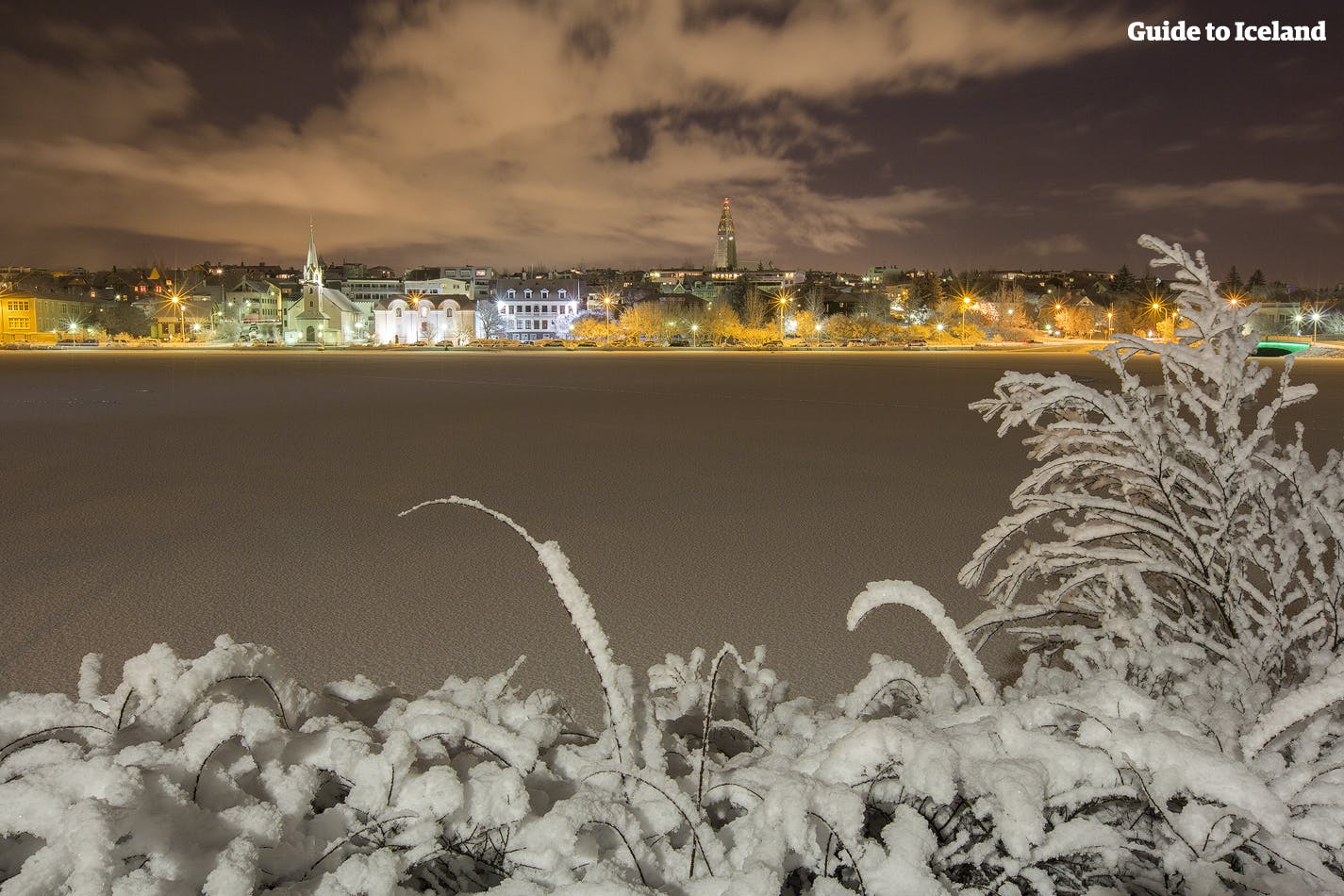 Zimowa noc w Reykjaviku, na horyzoncie ciepłe światła miasta.