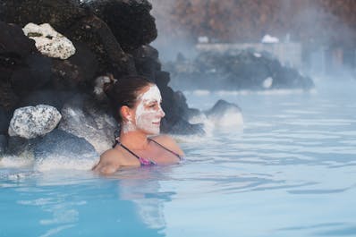 A woman has a face mask on as she relaxes in the waters of the Blue Lagoon geothermal spa.