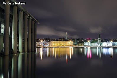 Die Lichter von Reykjavik spiegeln sich in der ruhigen Wasseroberfläche.