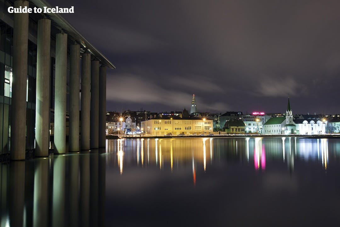 Die Lichter von Reykjavik spiegeln sich in der ruhigen Wasseroberfläche.