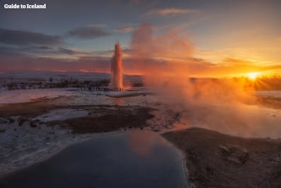 The Strokkur geyser erupts amid the otherworldly landscapes of the Geysir geothermal area at sunset.