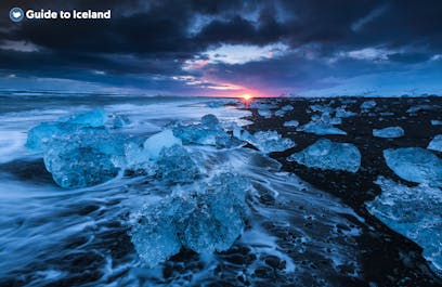 Huge ice chunks wash ashore at Diamond Beach, creating a surreal setting against the jet-black sands and a moody sky at sunset.