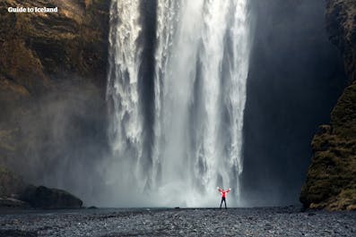 A person stands in front of Skogafoss waterfall on Iceland's South Coast, dwarfed by its size.