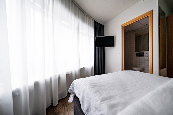A bed, white curtain by the window, and flat-screen TV in a hotel room at Center Hotels Klopp.