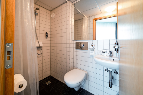 A bathroom at Center Hotels Klopp, with a toilet, basin, mirror, and shower.