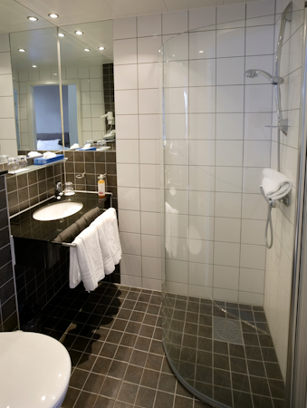 A bathroom with a shower, towels, and a hair dryer at Center Hotels Arnarhvoll.