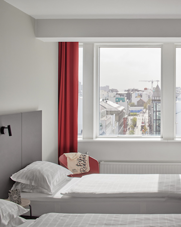 A bed with a pillow underneath a window with a city view outside.