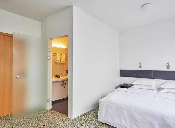 A bed in a hotel room with an open door leading into the ensuite bathroom.