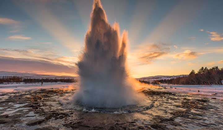 The beautiful Strokkur geyser erupts with the sun shining behind it.