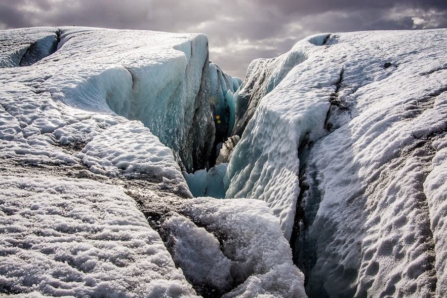 The movement of glaciers creates tensile strain on their brittle upper sections, causing them to break and create crevasses.